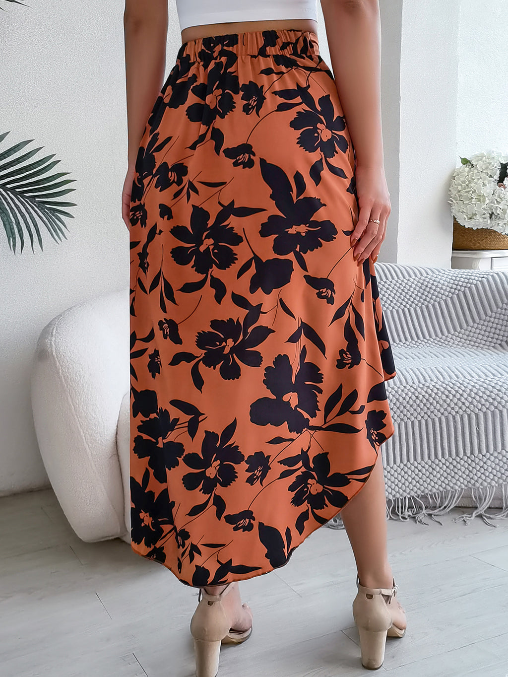 Person wearing an orange floral skirt in a room with a white couch and decorative items.