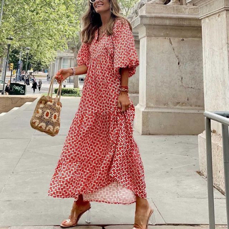 Woman in a red patterned dress holding a handbag on a city street.