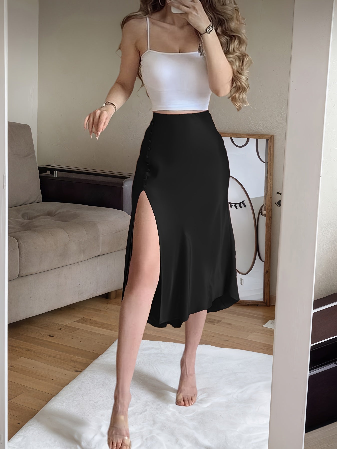 Woman wearing a white top and black skirt with a high slit, standing in a room.