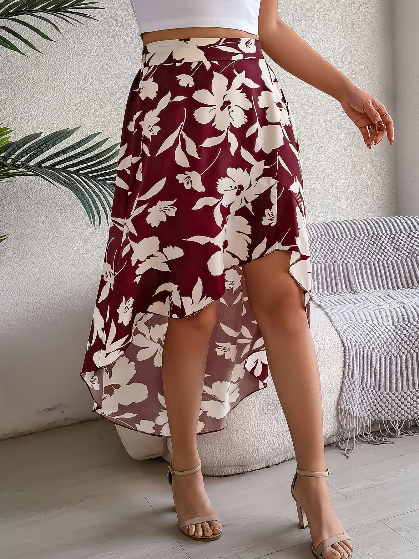 Person wearing a maroon floral skirt in a room with a couch and plant.