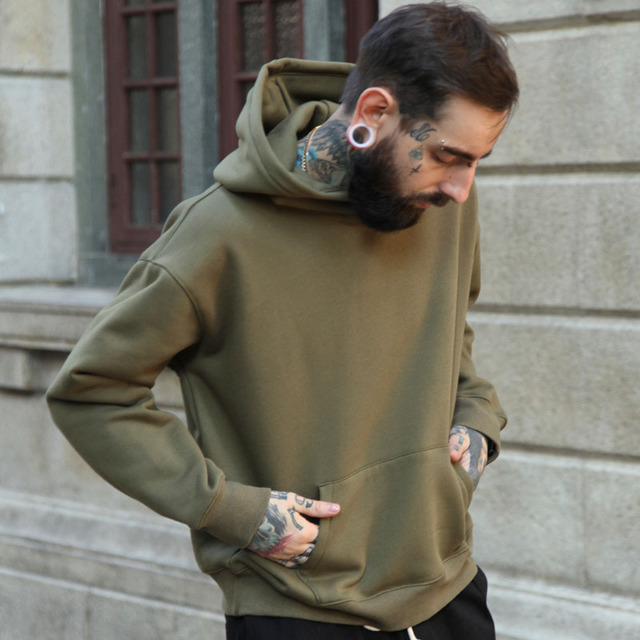 Man wearing a green hoodie standing against a stone building.
