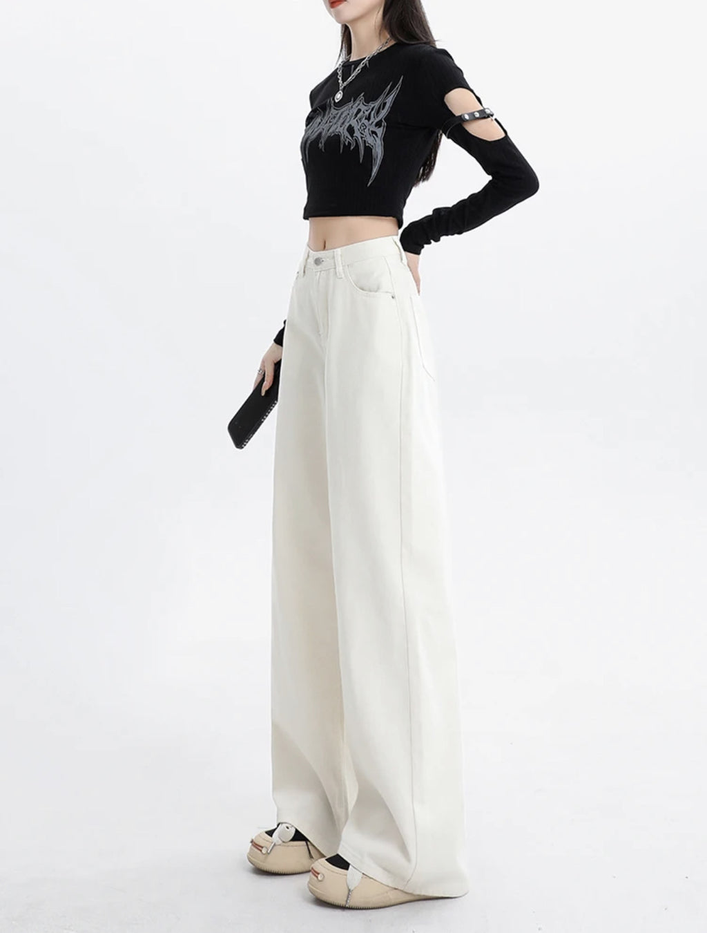 Person wearing a black crop top with cut-out sleeves and white wide-leg pants on a white background