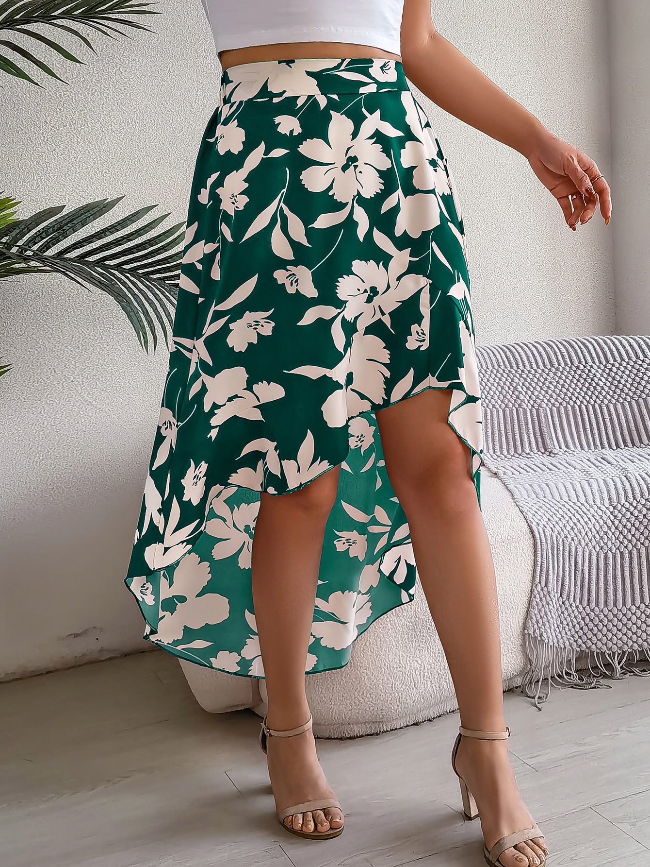 Person wearing a green floral skirt in a room with a couch and plant.