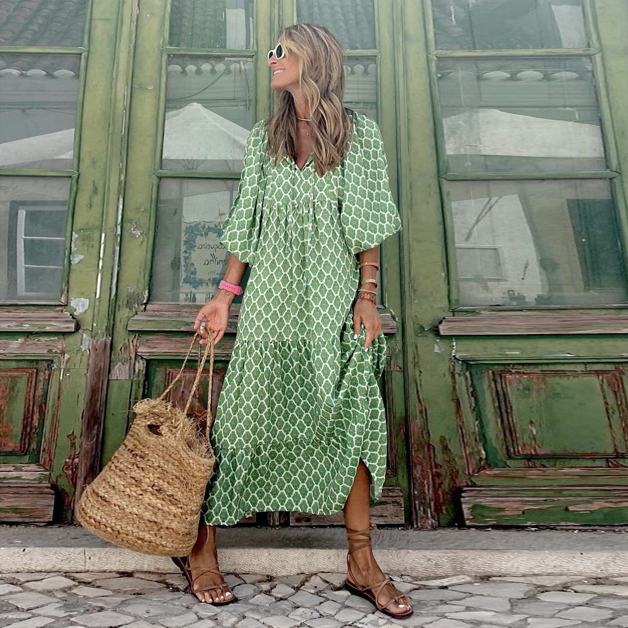 Woman in a green patterned dress standing in front of a green building.