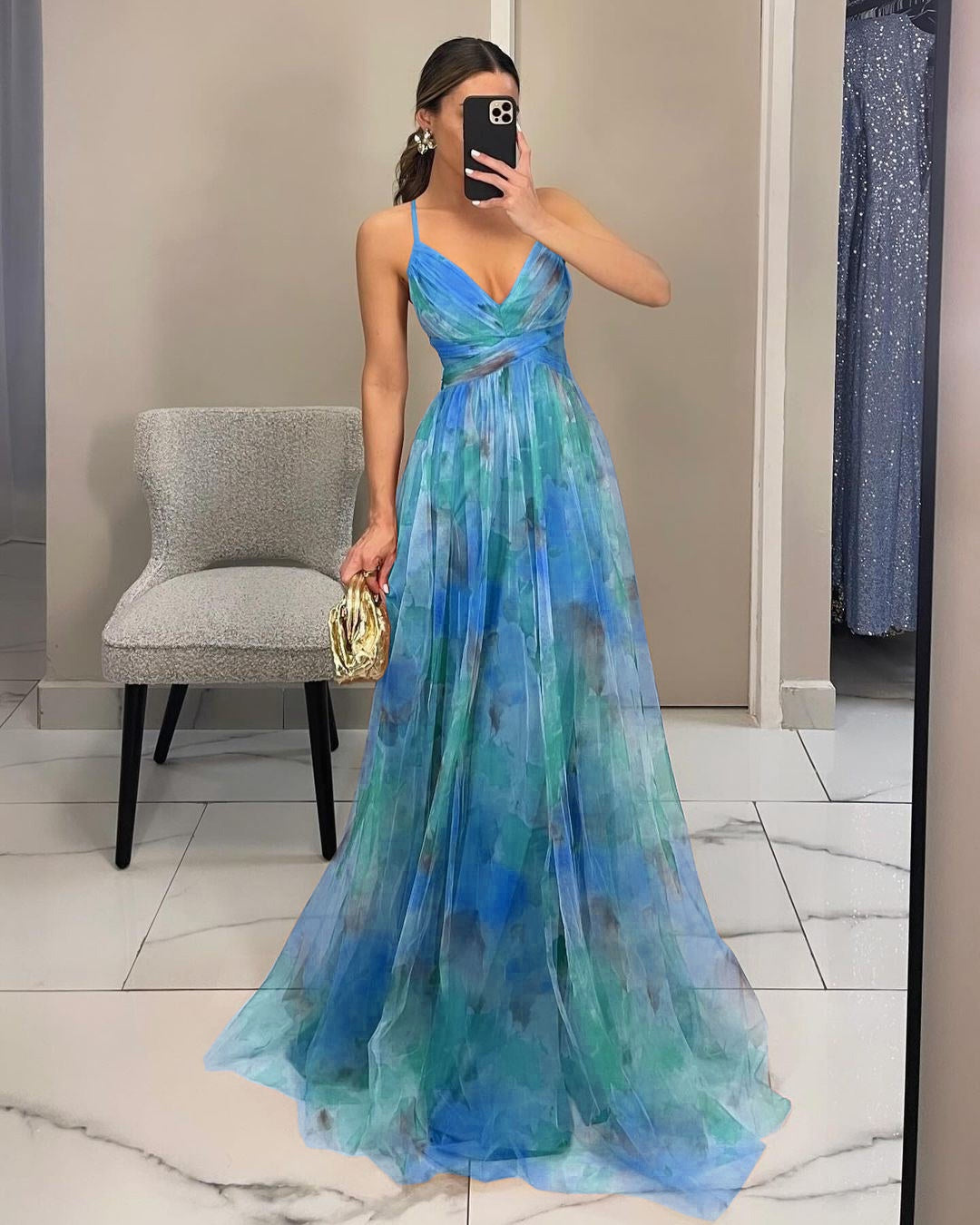 Woman wearing a blue and green floral dress taking a mirror selfie.
