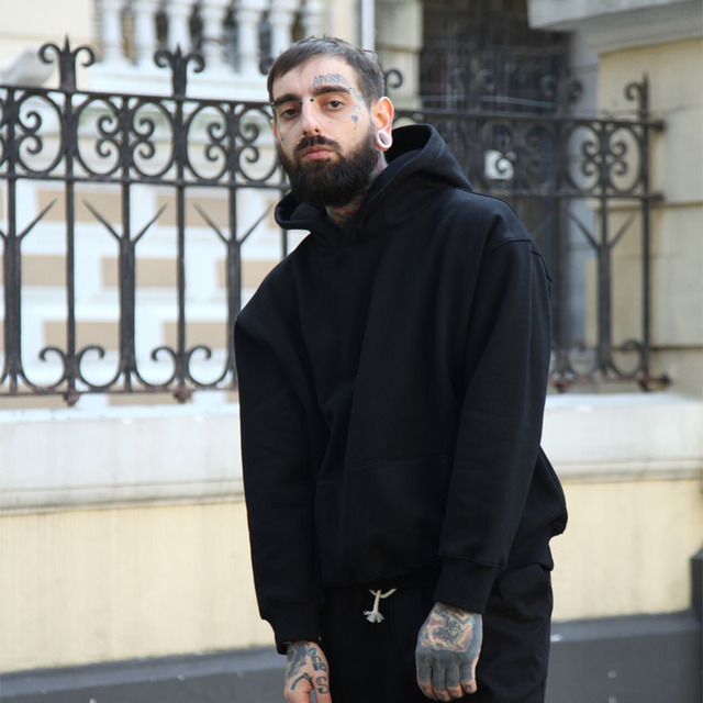 Man wearing a black hoodie standing in front of an iron gate.