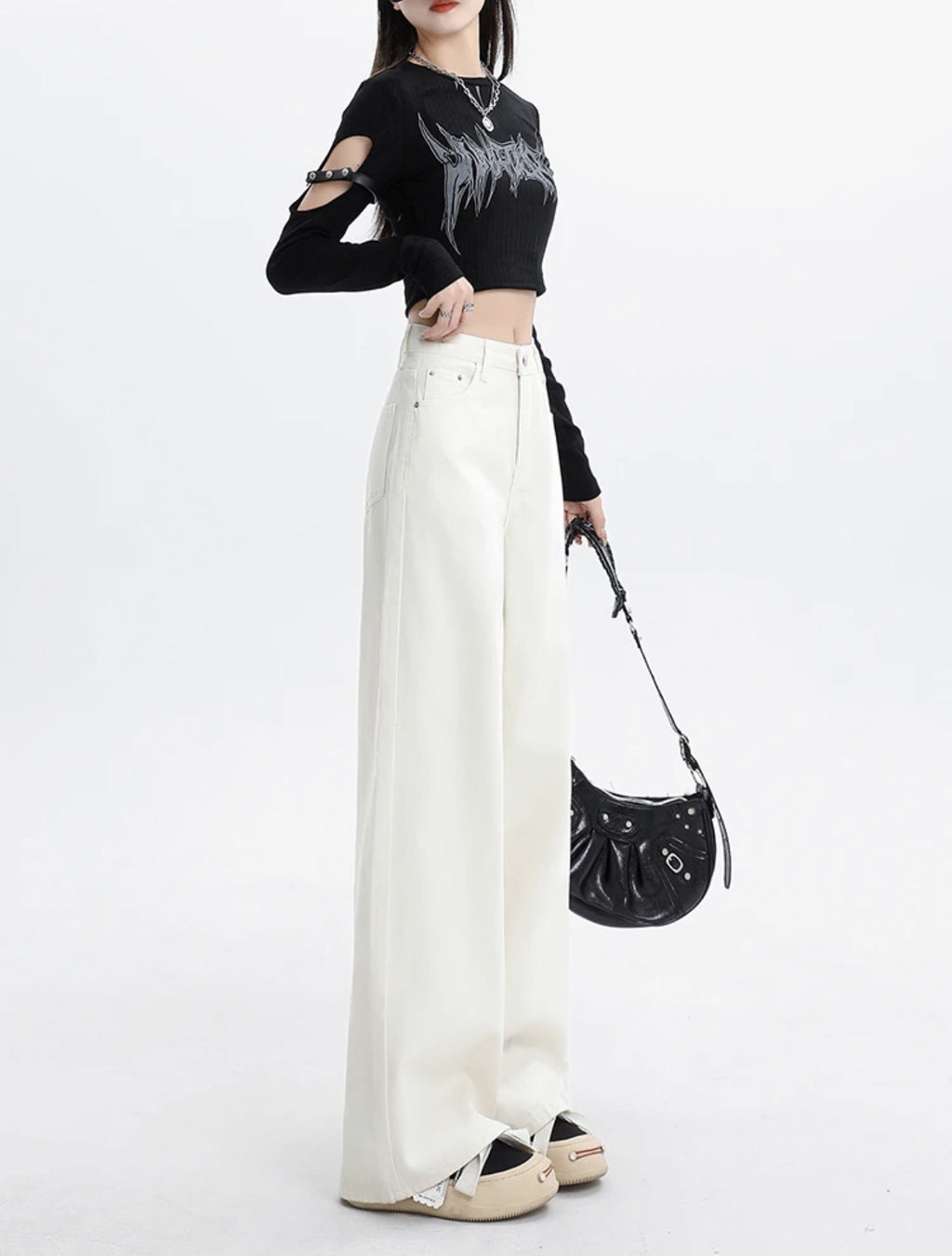 Person wearing a black crop top with cut-out design and white pants, holding a black handbag on a white background.
