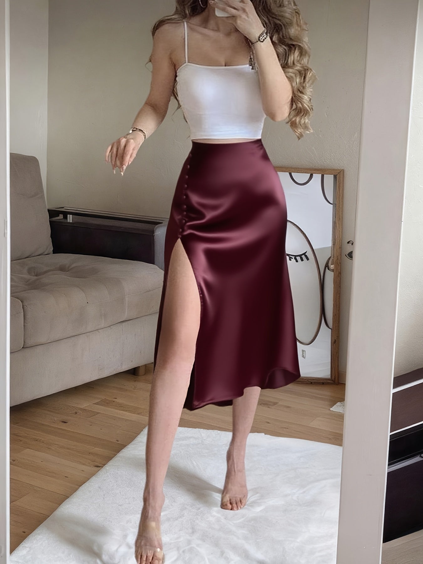 Woman wearing a white top and burgundy satin skirt in a room.