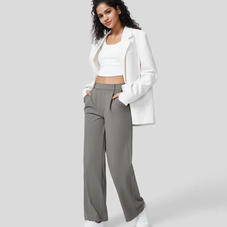 Woman wearing a white blazer and gray pants on a plain background