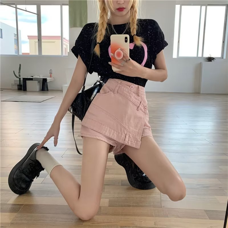 Person taking a mirror selfie wearing a black top and pink skirt in a room with large windows.