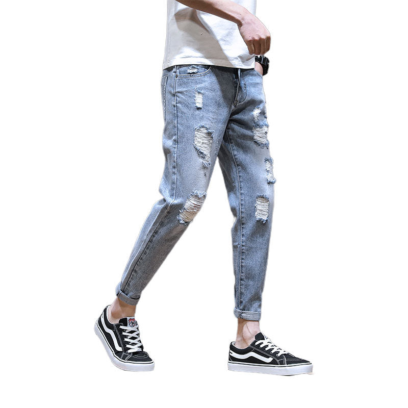 Person wearing light blue ripped jeans and black sneakers on a white background