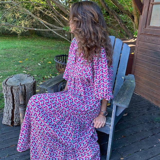 Woman in a patterned dress sitting on a wooden bench outdoors.