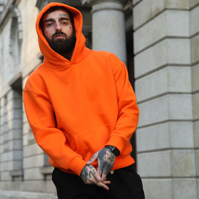 Man wearing an orange hoodie standing in front of a building