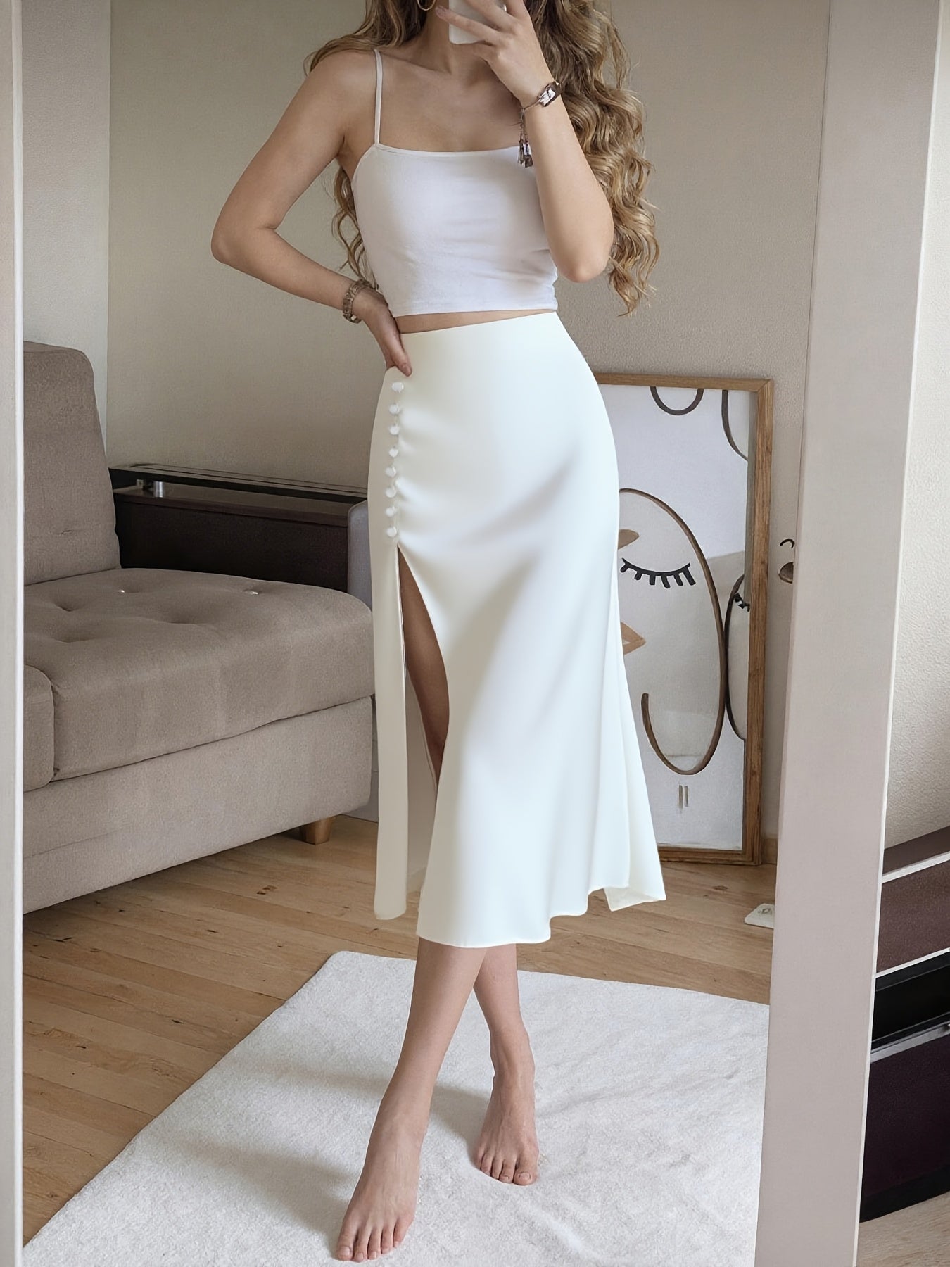 Woman wearing a white outfit with a slit skirt in a room.