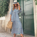 Woman in a blue and white patterned dress standing in front of a green door.