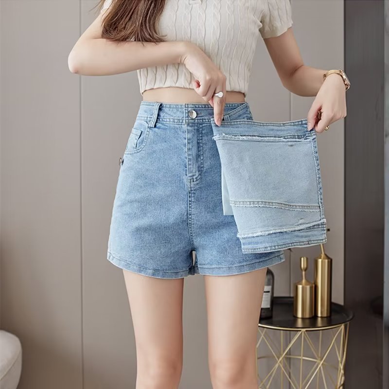 Person holding a folded pair of denim shorts in front of a neutral background